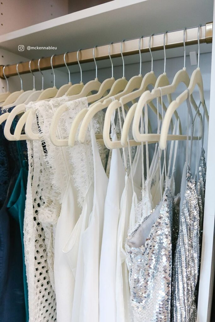 Cabides aveludados em tom claro organizam vestidos delicados em tons de branco e prata, incluindo rendas e paetês, criando um visual uniforme, elegante e funcional dentro do closet.